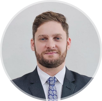 Foto de Julio Bento sorrindo, 
        usando terno e gravata, barba e fundo cinza